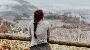 Girl leaning against a fence looking at a valley.