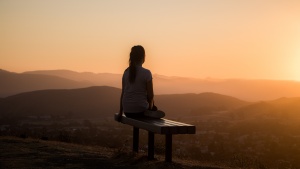 A woman sitting on a bench at sunset.