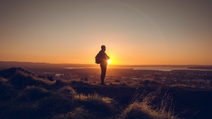 A man standing on a hill with the sun setting.