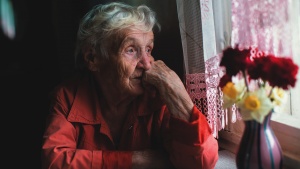 An older women sitting by a window looking outside.