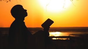 A person holding a Bible and looking up to the sky.