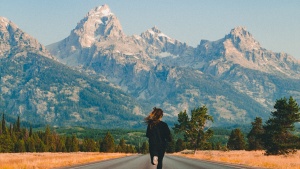 Photo of a person running towards mountains in the middle of an empty road.