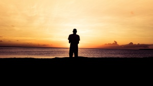 A person standing by a body of water at sunset.