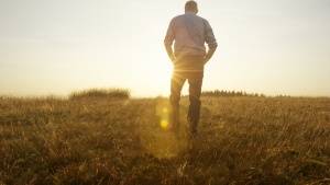 Photo of a man walking in a field toward the sun at golden hour.