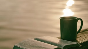 An open Bible lying on a table with a mug. 