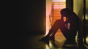 A sad woman sitting on the floor in a hallway.