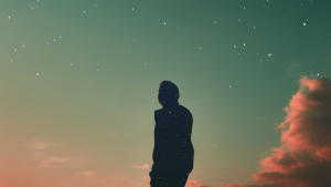 Silhouetted person against a dramatic, colorful sunset sky, with the person's silhouette filled with a different background, of a starry sky.