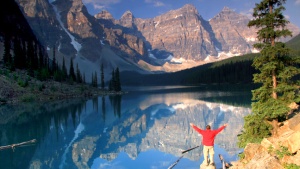 A man standing by a lake in the mountains.