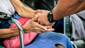 Photo of a younger person's hands gently holding an older person's hands on a subway.