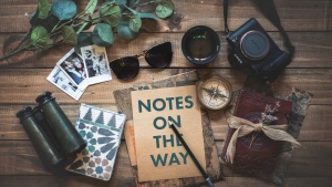 An assortment of items flat laid on a table, including a camera, a notebook, and sunglasses