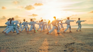 A group of people practicing martial arts moves on a beach.