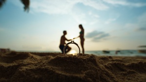 silhouette of man proposing to woman on a beach seen through a ring up close