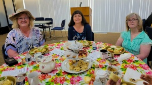 three ladies seated at a table enjoying tea and desserts