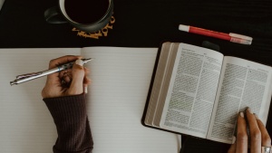 A pair of hands with a pen and an open Bible and blank notebook