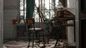 a desk and chair in a deteriorated room with the floor covered in old papers