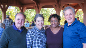 four people smiling and standing under a picnic shelter