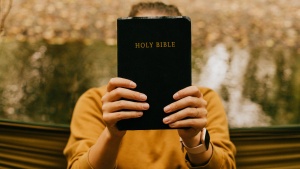 A woman holding a Bible in front of her face.