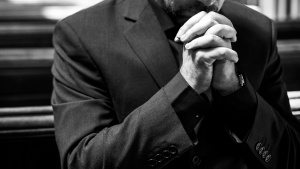 a man in a suit with hands folded in prayer