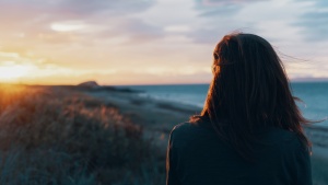 a woman standing with her back turned as she faces the sunset on the horizon