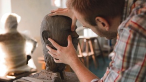 A sculpture forming a human head out of clay.
