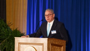 Len Martin standing at a podium with a blue curtained backdrop