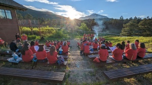 a large group of children seated on benches facing the sunset over the mountains in the distance