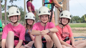 four girls wearing high ropes gear seated on the ground with smiles on their faces