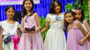 a group of five girls standing indoors and wearing pink and white dresses