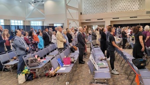 a meeting room full of standing people turned to the front of the room to sing hymns