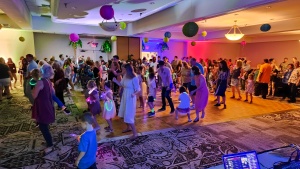 a large group of people dancing in a dimly-lit room with colorful lights and balloons