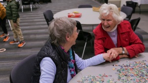 two ladies seated at a table covered with puzzle pieces