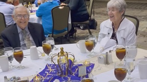 a senior man and woman sitting at a circular table in a banquet room with others seated in the background