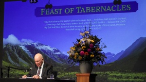 a man standing at the podium with a Feast of Tabernacles powerpoint presentation projected behind him