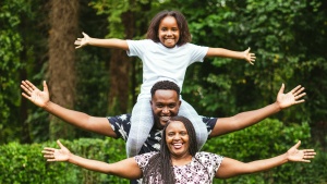 a man, woman, and child standing outdoors with outstretched arms and smiles