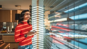 a woman standing indoors and looking out through a reflective window while holding a coffee cup