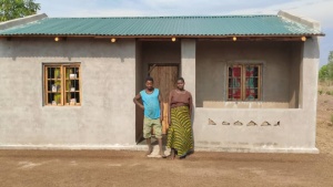 two people standing outdoors in front of a small building with a green roof