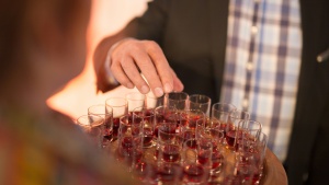 a man's hand reaching for a shot glass with red wine on a tray of similar glasses