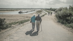 An elder couple walking together on a paved path.