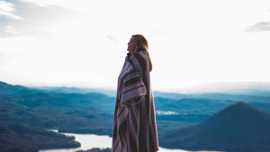 A woman wrapped in a blanket standing outside with mountains in the background.