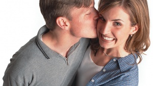 A young man kissing a young woman who is hugging him.