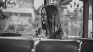 A young woman sitting by herself in a bus looking out the window.