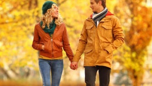 A man and woman holding hands walking in a park in the fall.