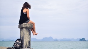woman sitting on post looking at water