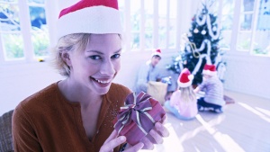 A woman wearing a red Santa hat and holding a gift.