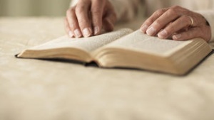 Older hands on top of a Bible.