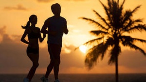 Man and woman running on beach with a palm tree in the background.