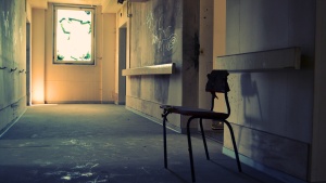 A lone student desk in a old run down school hallway.