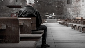 A old man sitting in a pew in an old church.