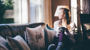 A young woman sitting on a couch looking out a window.