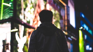 A man walking alone along a street surrounded by lit up signs.